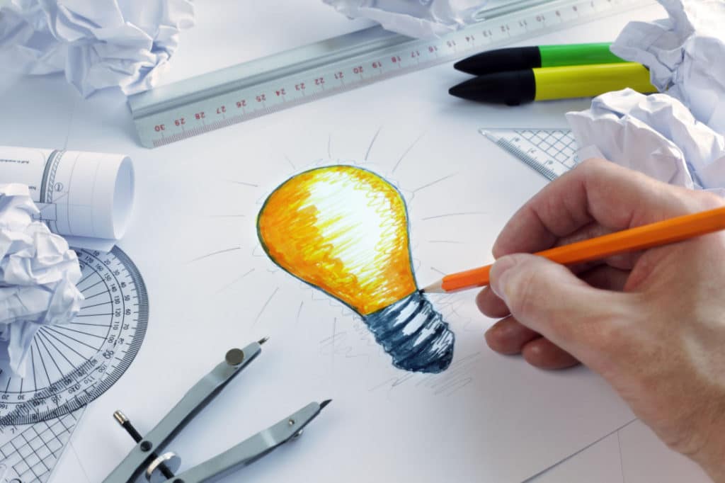 an artist draws a lightbulb using shades of yellow and orange on a black and white work station