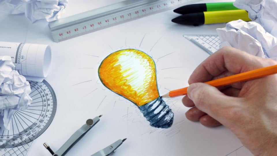 an artist draws a lightbulb using shades of yellow and orange on a black and white work station