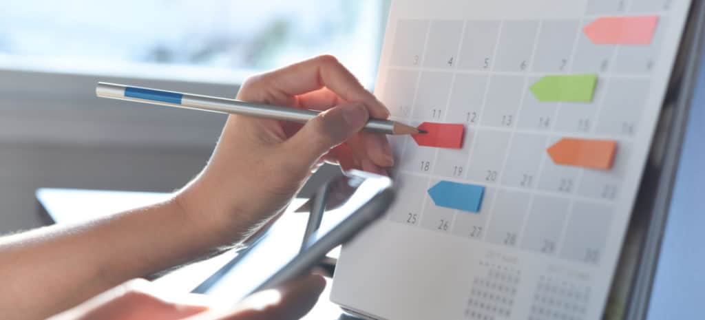 photo of hand using pen to write on organized calendar