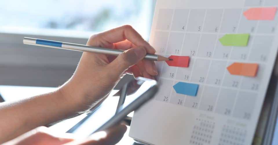 photo of hand using pen to write on organized calendar