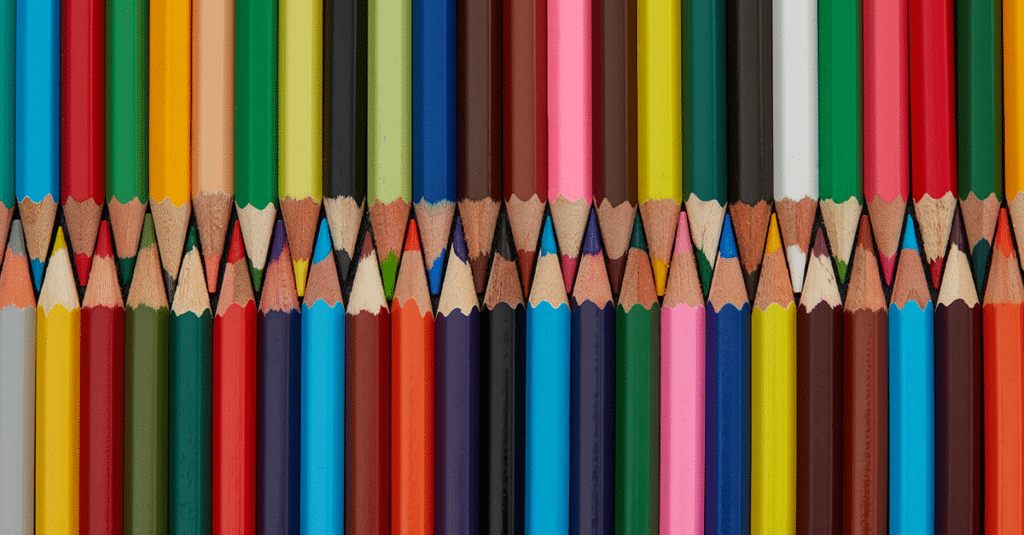 several colored pencils laid out on a table. The sharpened ends are fitted together as the top line of pencils points down and the bottom line of pencils point up