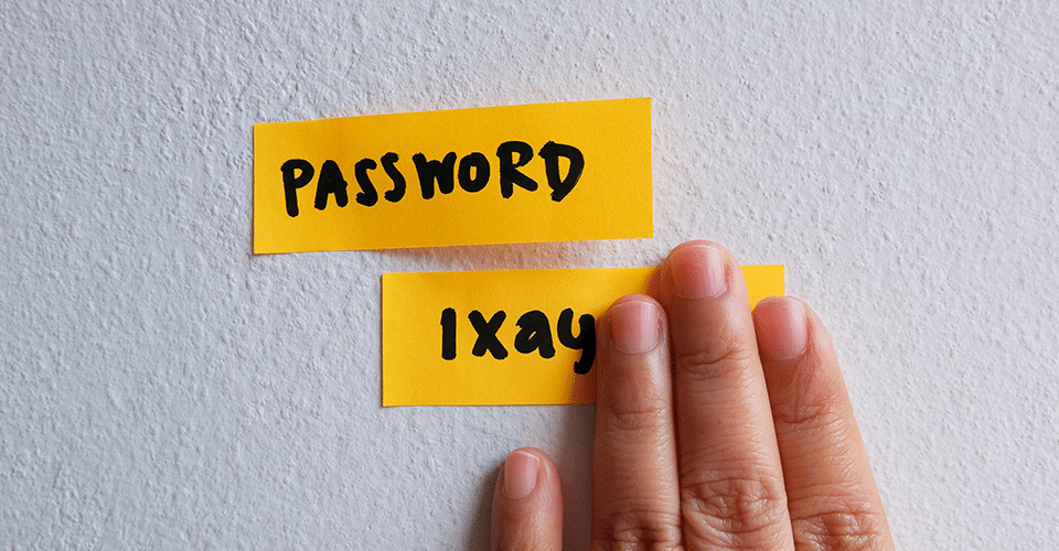 a yellow sticky note with the word Password. Below it is another yellow sticky note containing the password, but it's partially blocked by a hand