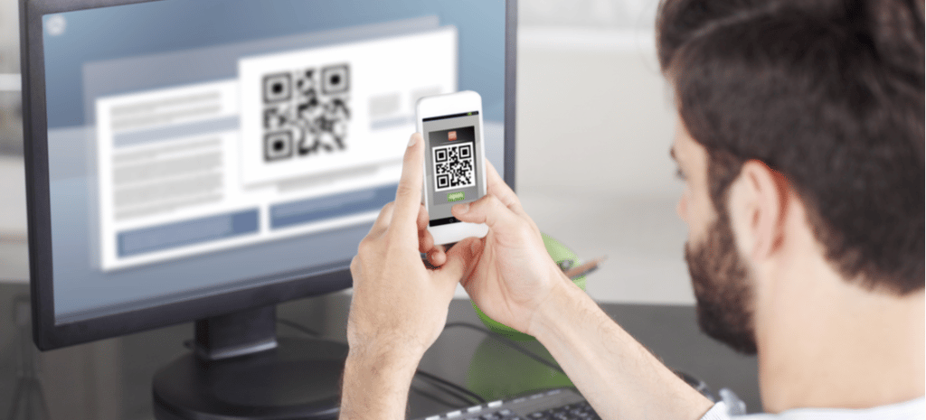 Man scanning QR code in front of a desktop monitor