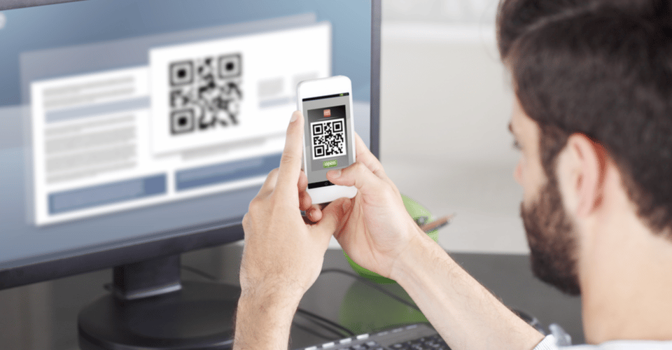 Man scanning QR code in front of a desktop monitor