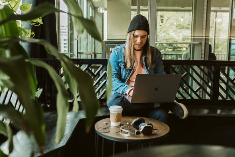 a man in a beanie works on a laptop in a coffee shop