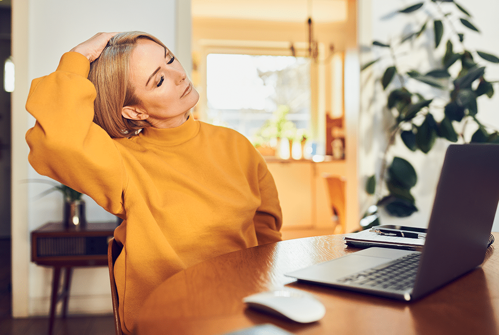 a woman in a yellow sweater takes a break by stretching at her desk