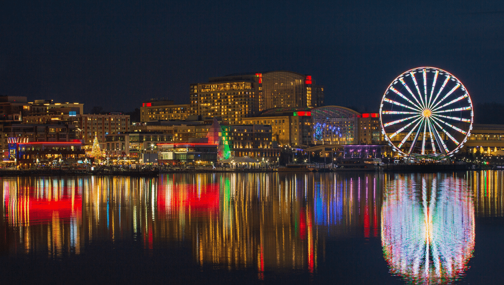 Night image of National Harbor, MD skyline which shows the ferris wheel and other landmarks lit up along the water