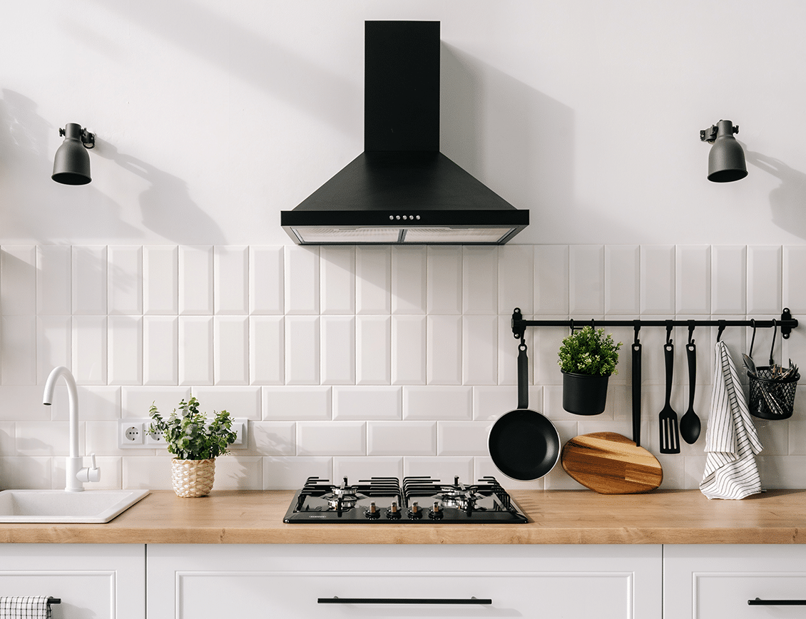 a bright white kitchen with a black vent hood and built-in cooktop