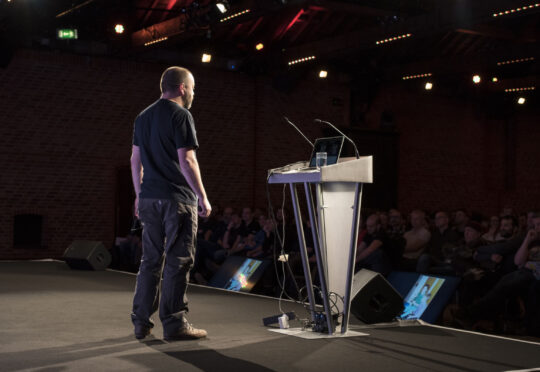 a presenter stands on stage at last year's PHP UK Conference